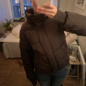 Brun pufferjacka - Säljer en brun pufferjacka med dragkedja och knappar. Jackan har långa ärmar och en hög krage för extra värme. Perfekt för kyliga dagar. Saken man hänger jackan med på krokar har gått sönder men det finns två så det är lungtt. Annars ganska bra skick, dock som en fläck vid sidan men inget jag tycker syns. Kan skicka bild🩵🩵 nypris 1000kr köpt för typ två tre år sedan så finns nog inte kvar❤️❤️