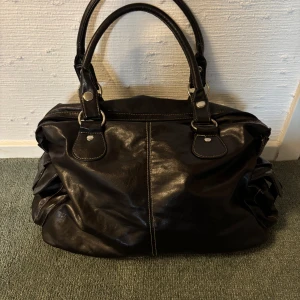 Brun axelväska i skinn - Snygg brun axelväska i skinn med praktiska handtag, rymlig och flera fack. Väskan har en stilren design med silverfärgade detaljer och en rymlig insida för alla dina saker.