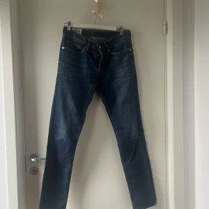 Blå jeans från Kings of Indigo - Snygga blå jeans från Kings of Indigo i modellen John med slim fit och lång midja. Klassisk femficksdesign med knappgylf och läderpatch baktill. Perfekta för en stilren look.