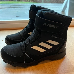 Svarta Adidas Terrex boots - Säljer ett par svarta Adidas Terrex vinterskor  Skorna är vattentäta med ClimaProof-teknologi. Perfekta för utomhusaktiviteter under kyligare säsonger. Storlek 38,5 