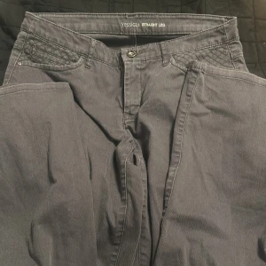 Grå byxor från Yessica - Snygga grå byxor från Yessica med straight leg design. De har klassiska femficksdetaljer och en knapp- och dragkedjestängning. Perfekta för en stilren look.