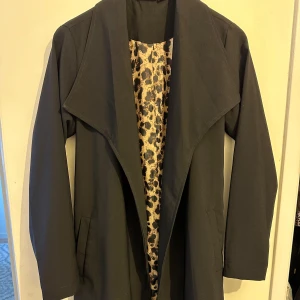Svart kappa från Esmara - Snygg svart kappa från Esmara med leopardmönstrat foder. Kappan har långa ärmar och ett knytbälte i midjan. 