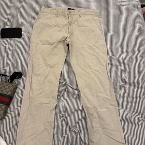Beige chinos från GANT - Säljer ett par stilrena beige chinos från GANT. Byxorna har låg midja och smal passform med knappstängning. Perfekta för en avslappnad men ändå uppklädd look.
