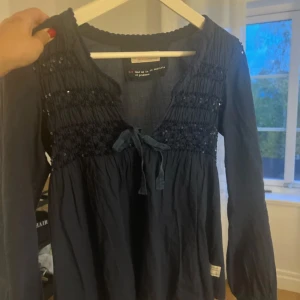 Odd Molly blus - Mörkblå långärmad topp från Odd molly med smockdetaljer och knytband framtill. 
