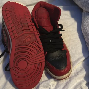 Nike Air Jordans i rött och svart - Snygga Nike Air Jordans i en klassisk röd och svart färgkombination. Skorna har en hög modell med snörning och en tydlig Nike-logga på sidan. Perfekta för dig som vill ha en stilren och sportig look.