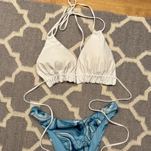 Vit och blå bikini med mönster - Snygg bikini med vit överdel och blåmönstrad underdel. Överdelen har knytband och rynkade detaljer, medan underdelen har ett coolt mönster i olika blå nyanser. Perfekt för sommarens stranddagar! Överdelen i storlek M. Nederdelen i storlek S/M. 50 för båda! Skickar inte bild med bikinin på!! 