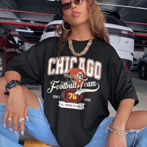 Svart t-shirt med Chicago-tryck - Cool svart t-shirt med stort tryck av 'Chicago Football Team' i vitt och rött. Perfekt för en avslappnad stil med en sportig touch. T-shirten har korta ärmar och en lös passform.