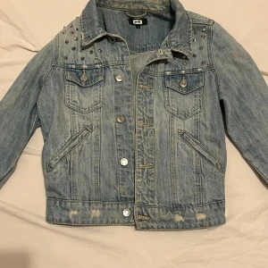 Jeansjacka med nitar från Bik Bok - Snygg jeansjacka från Bik Bok i ljusblå denim med coola nitar på axlarna. Jackan har knappar framtill och två bröstfickor med lock. Perfekt för en trendig look! Använd par gånger man ser det på bilderna