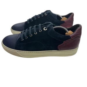 Svarta sneakers med vinröda detaljer - Ett par snygga svarta Lanvin sneakers med vinröda detaljer och beige sula. Skorna har snörning och en stilren design som passar perfekt till vardags. De är tillverkade i ett material som ger en lyxig känsla. Nypris ligger på 4999 kr