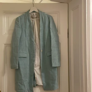 Ljusblå kappa från Zara - Elegant ljusblå kappa från Zara med en stilren design. Kappan har långa ärmar och en enkel knäppning framtill. Perfekt för vår och höst med sin lätta och bekväma passform. Tyget liknar linne.
