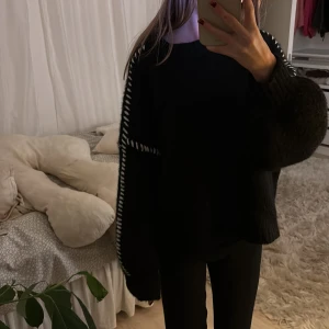 Svart stickad tröja med vita detaljer - Mysig svart stickad tröja med vita detaljer längs ärmarna. Perfekt för kyliga dagar med sin avslappnade passform och långa ärmar. En stilren och bekväm tröja för alla tillfällen.