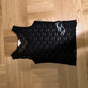 Svart spetslinne från Gina Tricot - Snyggt svart spetslinne från Gina Tricot i storlek 140. Perfekt för en stilren look med sitt genombrutna spetsmönster. Linnet är ärmlöst och passar bra till både vardag och fest.