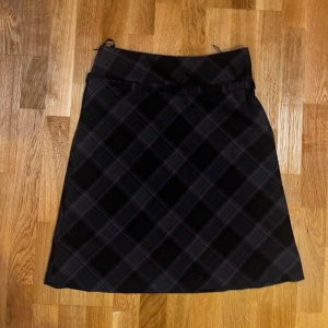 Svart rutig kjol - Snygg svart rutig kjol med klassiskt mönster. Perfekt för en stilren look. Kjolen har en A-linjeformad passform och är knälång.