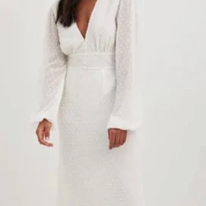 Vit maxiklänning med detaljer  - Vit långklänning från NA-KD med diskret prickigt mönster. Klänningen har en v-ringad design och långa ärmar. Oanvänd.