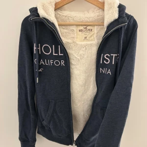 Mysig & mjuk kofta från Hollister - Mysig mörkblå hoodie från Hollister med fluffigt foder och dragkedja. Perfekt för kalla dagar. Använd fåtal gånger så är som gott som ny & Inga defekter!
