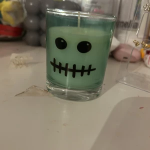 Grönt ljus med dödskallemotiv - Säljer ett grönt ljus i glasbehållare med ett coolt dödskallemotiv. Perfekt för att skapa en mysig och lite läskig stämning hemma. Ljusets design är både rolig och unik, vilket gör det till en utmärkt dekoration.