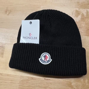 Svart ribbad mössa från Moncler - Säljer 1 för 600kr, 2 för 1000kr, 3 för 1400kr. Snygg svart ribbad mössa från Moncler med broderad logotyp framtill. Perfekt för att hålla värmen under kyliga dagar.  PRIS KAN DISKUTERAS!!!