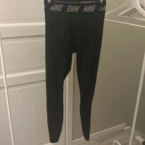 Svarta leggings från Nike - Säljer ett par svarta Nike leggings i storlek S. De är i mycket bra skick och har en elastisk midja med Nike-loggan runtom. Perfekta för träning eller vardagsbruk. Materialet är mjukt och stretchigt för bästa komfort.