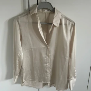 Beige sidenblus från Mango - Säljer en elegant beige blus i siden från Mango! Den har en klassisk krage och knappar framtill. Perfekt för både vardag och festliga tillfällen. Blusen har långa ärmar och en mjuk, lyxig känsla. Passar perfekt till både jeans och kjol!