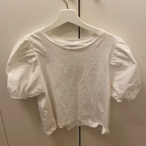 Vit topp från Zara - Säljer en söt vit topp från Zara i storlek S. Den har puffiga kortärmar och en rund halsringning. Perfekt för sommardagar eller en avslappnad vårlook. Toppen är i bra skick och gjord av mjukt material.