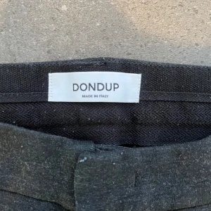 Svarta byxor från Dondup - Säljer ett par svarta byxor från Dondup, tillverkade i Italien. De har en stilren design med en smal passform och knappar bak. Perfekta för både vardag och fest. Byxorna är i bra skick och redo för en ny ägare!