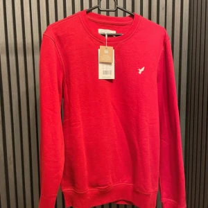 Röd tröja från Pier One - Säljer en snygg röd tröja från Pier One i storlek XS. Den har en liten broderad fågel på bröstet och är gjord av mjukt material. Perfekt för både vardag och fest! 🔥