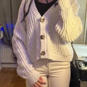 Vit stickad kofta med stora knappar - Mysig vit stickad kofta med stora, snygga knappar framtill. Perfekt för kyliga dagar och ger en avslappnad look. Koftan har en loose passform och långa ärmar, vilket gör den superbekväm att bära. Passar perfekt till både jeans och kjol!