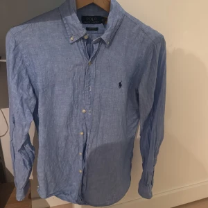 Blå skjorta från Ralph Lauren - Säljer en snygg blå skjorta från Ralph Lauren i storlek Custom Fit. Skjortan är långärmad och har en klassisk krage med knappar. Perfekt för både vardag och fest! 