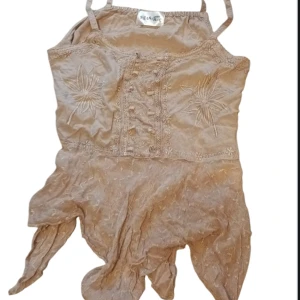 Beige linne med broderade detaljer - Säljer ett unikt beige linne från sol&måne med broderade blommor och knappar framtill. Toppen har smala axelband och en asymmetrisk nederkant som ger en bohemisk känsla. 