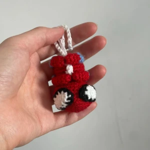 Handgjord “bag friend” - Söt handgjord nyckelring i form av en röd figur med vita och svarta detaljer. Den är virkad och har en liten blå detalj på toppen. Perfekt att hänga på väskan. Unik och charmig accessoar för att ge lite personlighet till dina saker!