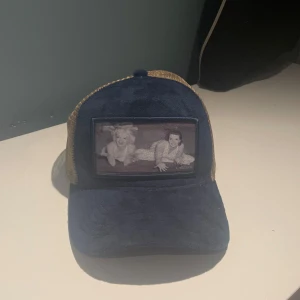 Blå och beige velvet keps - Säljer en cool keps i blått och beige med ett nätmaterial på baksidan. Framsidan har en unik bilddetalj som ger kepsen en personlig touch. Justerbar passform för att passa de flesta huvudstorlekar. Och köpt för 419kr.