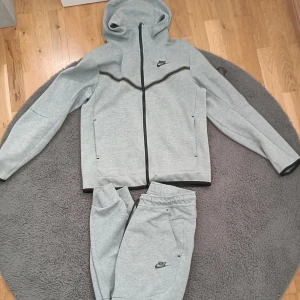 Grå Nike Tech  - Grå Nike tech. Storlek S på tröjan och M på byxorna. Har en liten missfärgning på tröjan. Visas på bilderna. Men syns inte särskilt tydligt. Inga skador och sparsamt använd