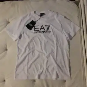 Säljer en snygg vit t-shirt från Emporio Armani med EA7-logga på bröstet. Den är kortärmad och i nytt skick . Passar både till vardags och festliga tillfällen. Helt ny med tag kvar! Märket glimrar även när den är i starkt ljus. S i storlek.