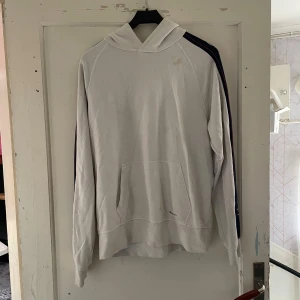 Vit hoodie från GANT - Säljer en snygg vit hoodie från GANT med långa ärmar och en klassisk känguruficka. Den har en stilren design med GANT-loggan tryckt på ärmarna och framtill. Perfekt för en avslappnad stil eller för att hålla sig varm under kyliga dagar. Passar både till vardags och träning!