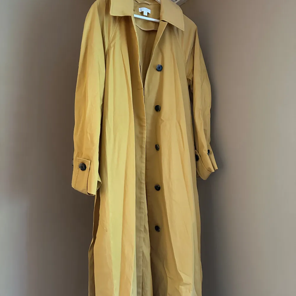 Säljer en superfin gul trenchcoat från COS i storlek M. Den har en klassisk design med stora knappar och långa ärmar. Perfekt för vår och höst när du vill ha något stilrent och bekvämt. Jackan är i bra skick och redo för nya äventyr!. Jackor.