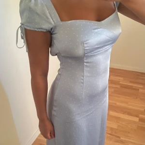 Prickig blå lång klänning i satin  - Prickig blå klänning i satin. Använt en gång. Har öppen rygg men en knytning. Knytning på ärmarna 