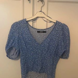 Blå blommig topp från BikBok - Säljer en superfin blå topp från BikBok i storlek XS. Den har ett sött blommigt mönster och korta puffärmar. Toppen är perfekt för vår och sommar och har en v-ringad design. Den är endast använd ett fåtal gånger och är i ett mycket fint skick 💕💕