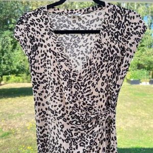 Leopardklänning - En leopardklänning från Indiska i storlek XS 🐆 Säljer pga att den inte används längre! Klänningen har en fin knytning i midjan, omlott, v-ringning samt går ner till knäna 🤍🤎  True to size!  Längd: 98 cm Axel: 47 cm Midja: 61 cm