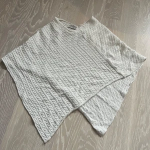 Vit stickad poncho från Hampton Republic - Säljer en superfin vit stickad poncho från Hampton Republic. Den har ett snyggt flätmönster och är perfekt för höst och vinter. Ponchon är i super skick och passar perfekt för att hålla sig varm och stilren. Perfekt att slänga över en tröja!