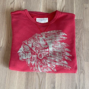 Röd tröja med tryck från Ralph Lauren - Tröja från Ralph Lauren Denim med ett stort tryck av en huvudbonad på framsidan. Tröjan är långärmad och perfekt för en avslappnad stil. Den är i superskick 10/10 kvalite, köpt för flera år sen använd 1 gång bara. Nypris 1000kr. Mitt pris 129kr.