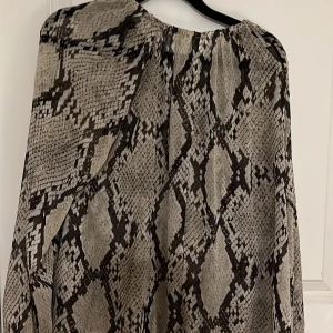 Ormmönstrad blus - Snygg blus med ormmönster i svart och grått. Den har en lös passform och är perfekt för en trendig look. Materialet är lätt och luftigt, vilket gör den bekväm att bära.
