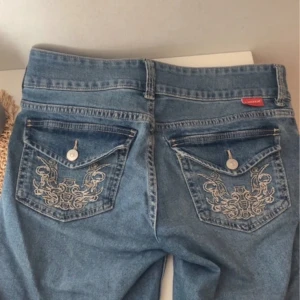 Blå jeans med broderade fickor - Snygga lågmidjade flare jeans från H&M. Sparsamt använda men ett litet hål vid ena fickan som är igensytt, inget man tänker på när man har på sig de💗