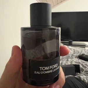 Tom Ford Eau d'Ombre Leather - Säljer en elegant parfym från Tom Ford, Eau d'Ombre Leather. Flaskan är stilren och mörk med en svart etikett och svart lock. Perfekt för den som gillar en sofistikerad doft med lädertoner och vanilj. 