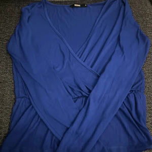 Blå omlottopp från BikBok - Snygg blå omlottopp från BikBok med långa ärmar. Perfekt för en stilren look. Toppen har en v-ringad design och är tillverkad i ett mjukt material 💓