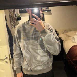 Grå mönstrad tröja från Iets Frans - Säljer en grå tröja från Iets Frans med ett unikt abstrakt mönster. Tröjan har långa ärmar och ribbade muddar vid ärmslut och nederkant. Perfekt för en stilren och modern look. Storleken är M och är köpt från Urban Outfitters för ca 2 år sedan. Modellen är 187 cm lång. Tröjan är 67 cm lång. Tröjan är i mycket bra skick och har inga skador.