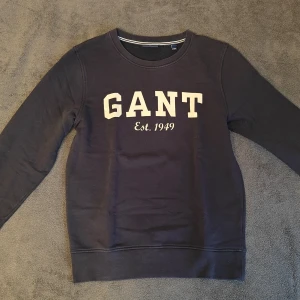 GANT tröja - Säljer en klassisk svart sweatshirt från GANT med tryck på framsidan. Tröjan har rund hals och långa ärmar. Härlig marinblå färg, i storlek Small och 100% bomull. Hör av dig vid frågor eller funderingar! 