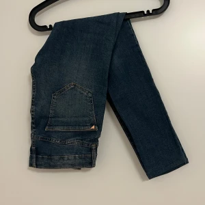 Blå jeans från River Island - Snygga blå jeans från River Island med slitna detaljer på benen. Perfekta för en avslappnad stil. Klassisk femficksdesign och knappgylf.