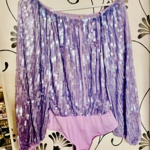 Lila paljettbody - Säljer en glittrig lila body med paljetter och långa ärmar. Perfekt för en festlig kväll! 💜NY oanvänd 