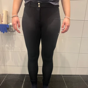 Svarta ridbyxor från ZacZess - Snygga svarta ridbyxor från ZacZess i storlek S. Byxorna har hög midja och en tight passform med praktiska fickor och dragkedja. Perfekta för ridning med stilren design. 