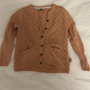 Beige/rosa kofta från Little Pomp de Lux - Säljer en söt beige/rosa blandat med orange kofta från Little Pomp de Lux. Koftan har ett fint stickat mönster och knappar framtill. Perfekt för lager-på-lager under svalare dagar. Den kommer tvättas och strykas innan den skickas! ⭐️